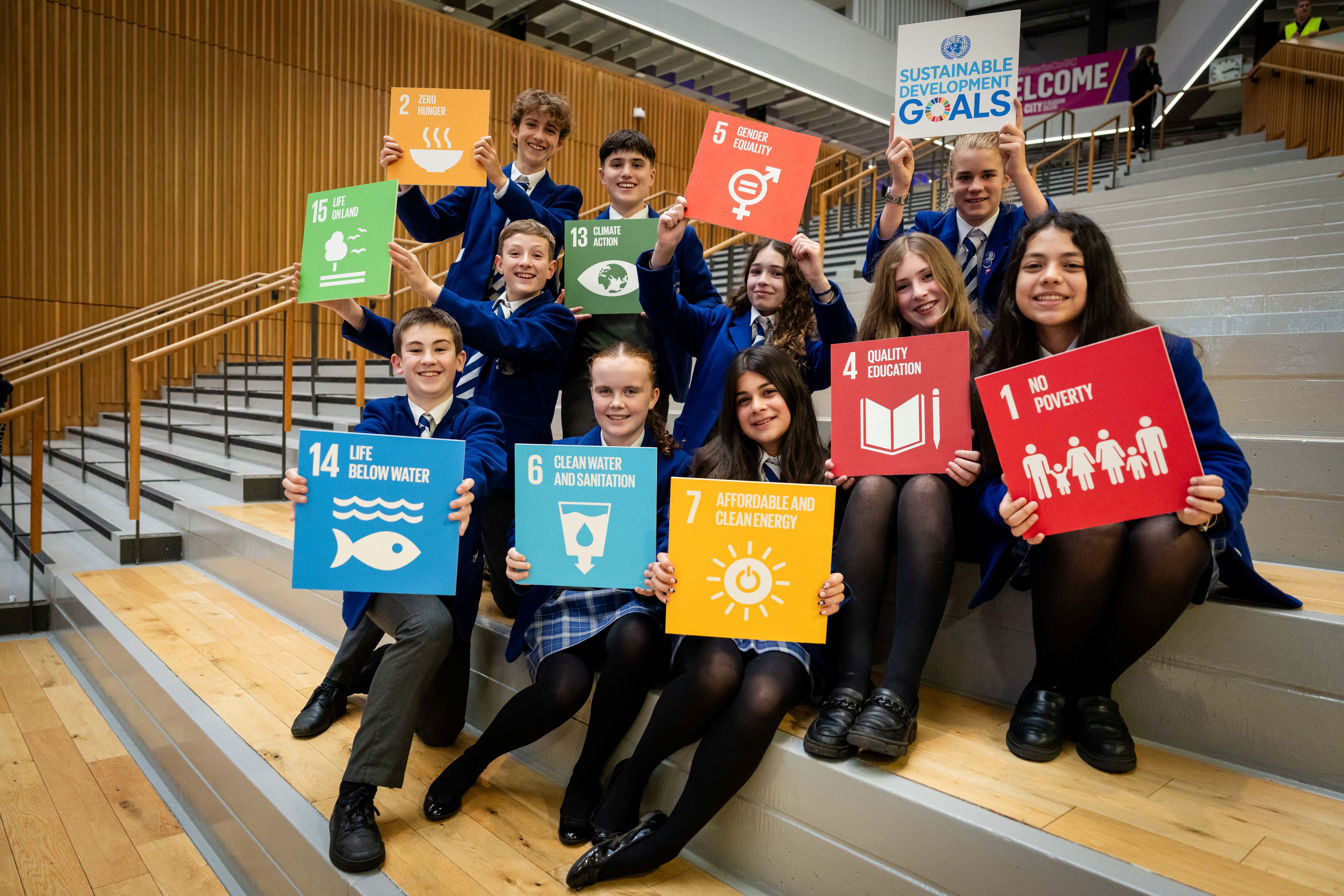 Students pose on stairs holding UN Sustainable Development Goals signs