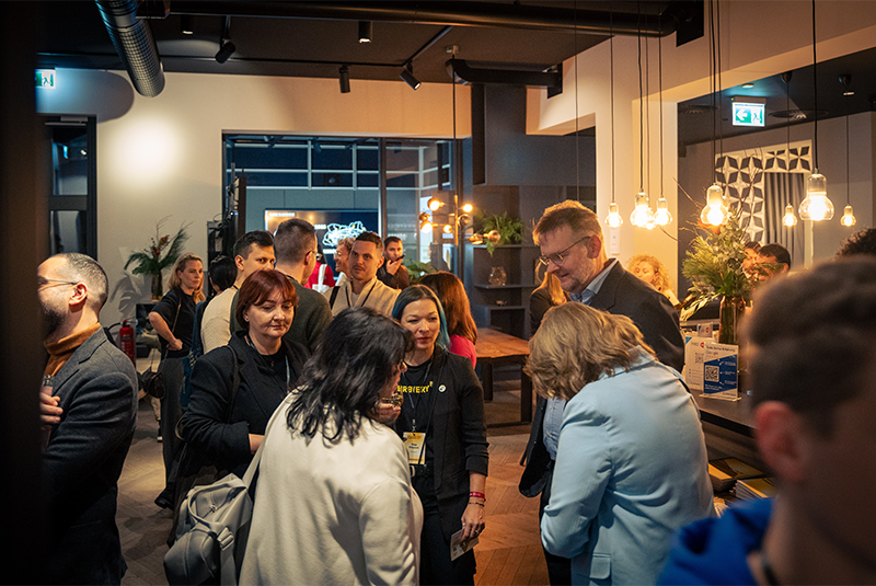 Man in a suit holding a microphone and smiling, with a woman beside him smiling as well during a panel discussion.