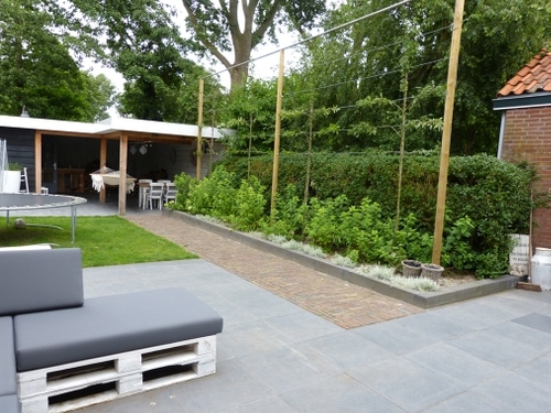 De lange, iets verhoogde border met bol hortensia's en leibomen begeleidt het klinkerpad.