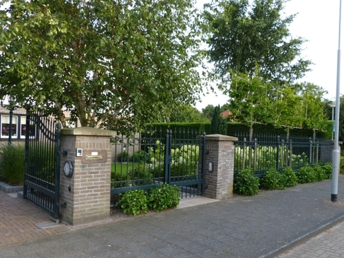 Leibomen en struikhedera achter het mooie hek van deze voortuin.