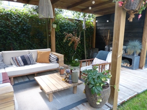 De lounge hoek gezellig ingericht onder de overkapping zonder achterwand met een vloer van steenschotten.