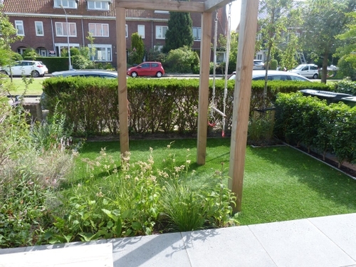 Een rekstok en een trapeze boven kunstgras in de voortuin.