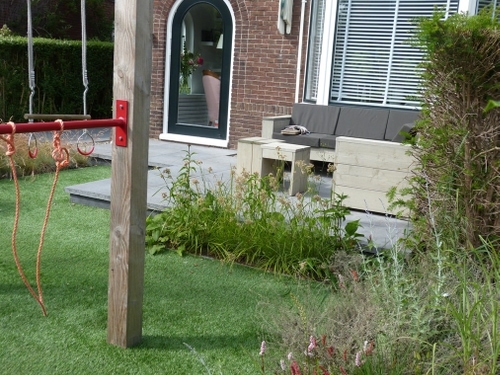 Het speeltoestel in de voortuin, achter het verhoogde terras met loungebank.