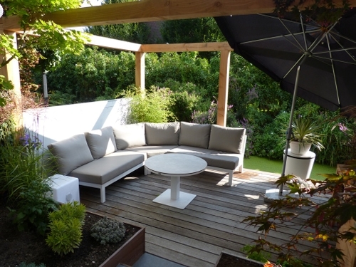 Een ronde loungebank met een in hoogte verstelbare salon - eettafel onder een zelf gebouwd pergola met gestucte muurtjes.