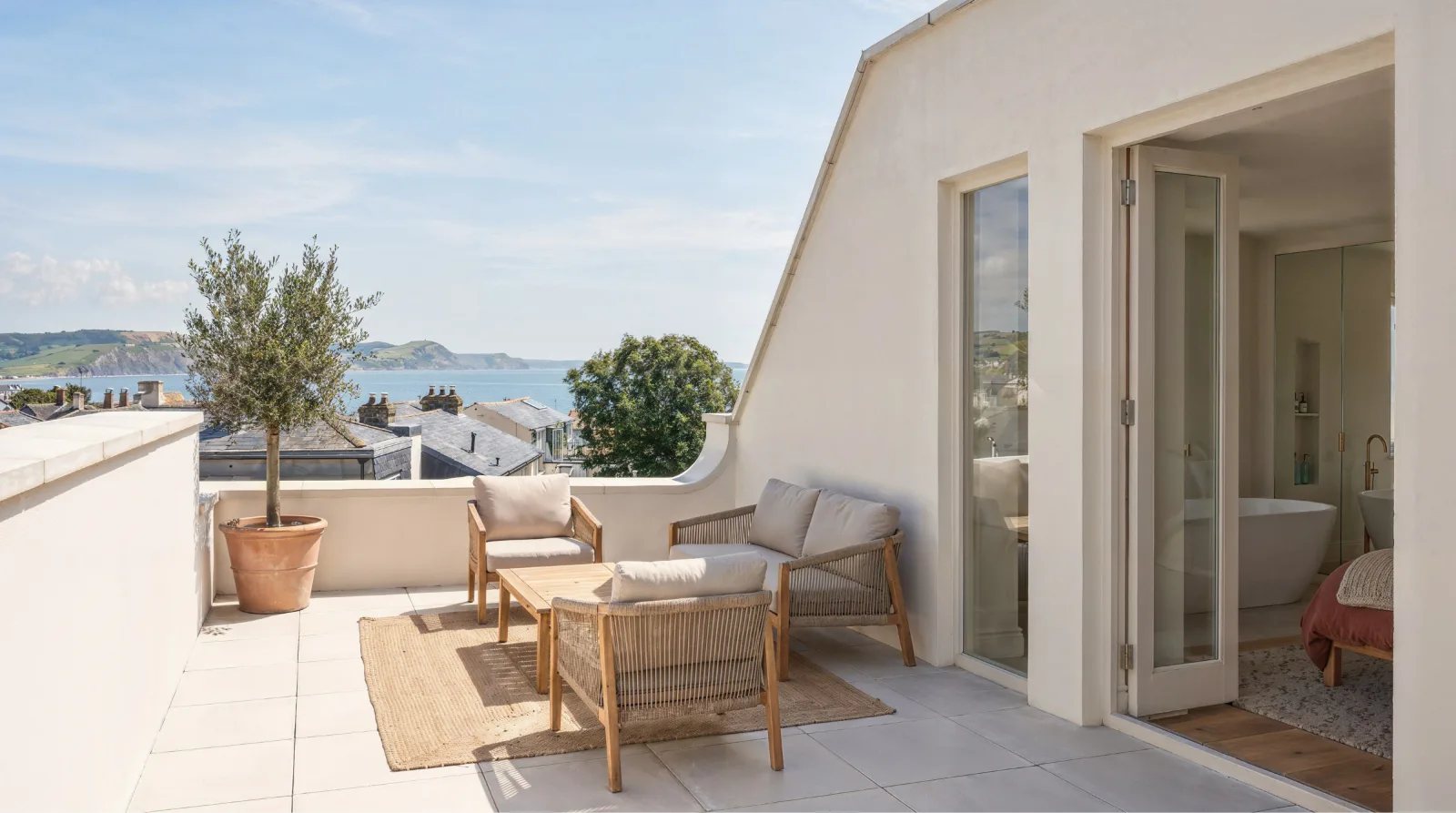Roof terrace with outdoor seating, an olive tree and a view of the bay