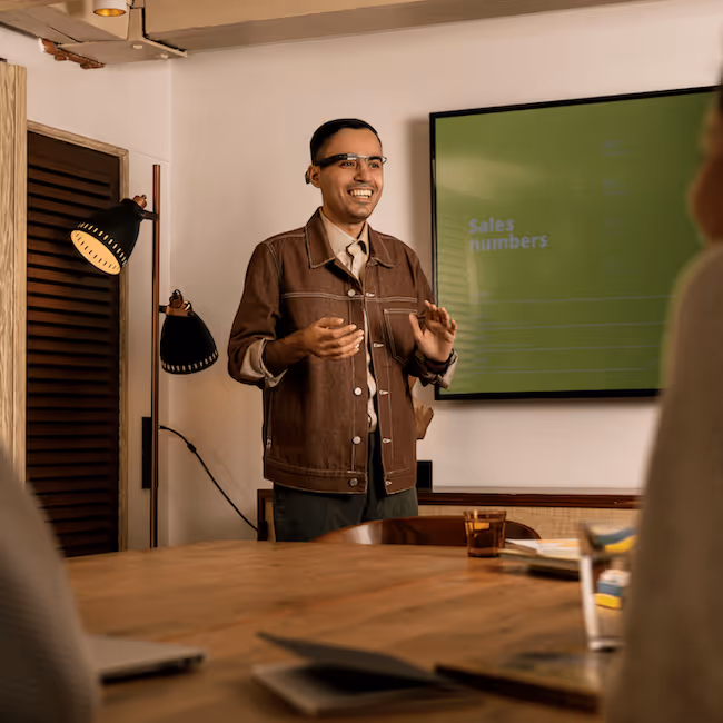 A photo taken inbetween two people watching a person giving a presentation that is wearing the Envision Glasses