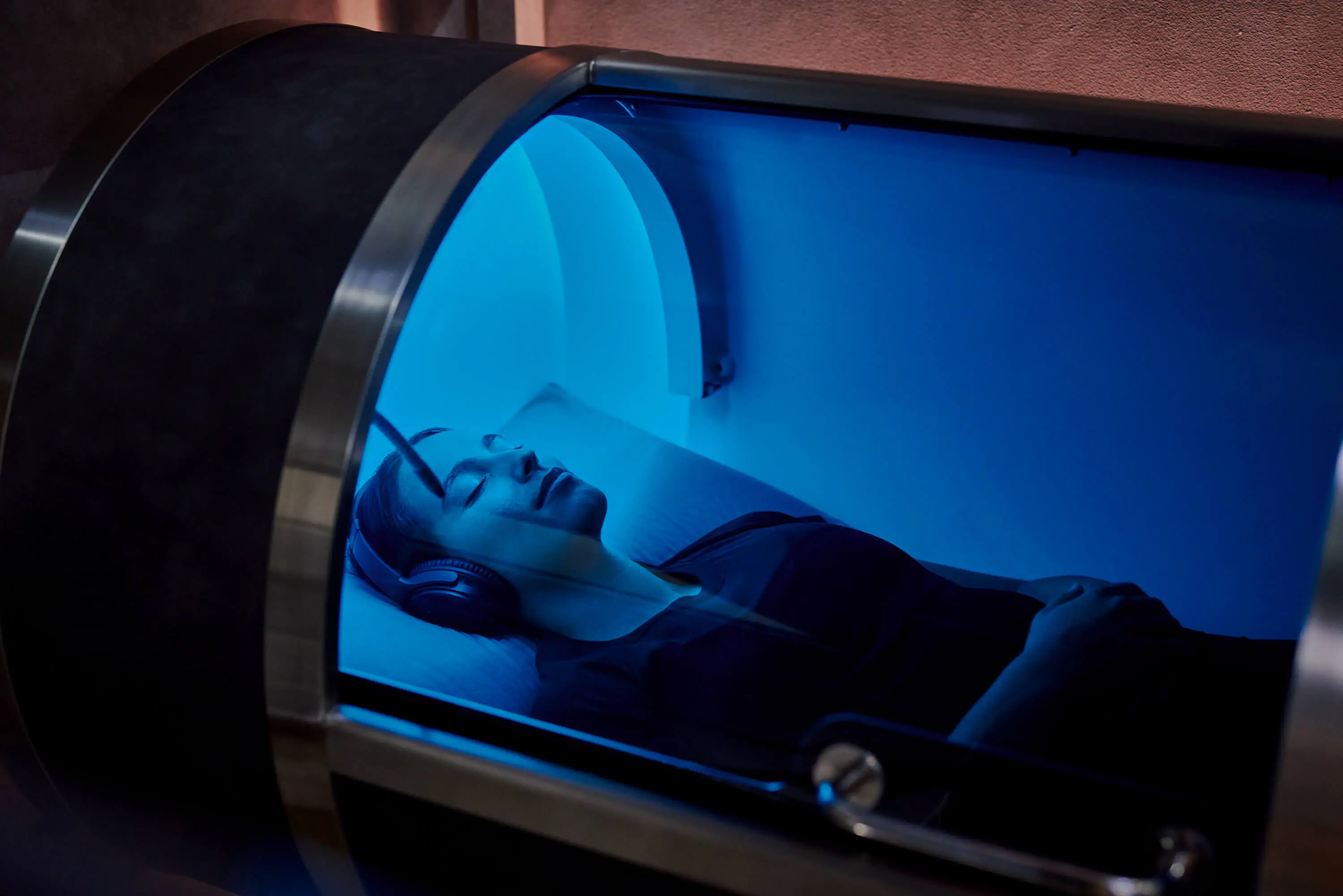 Interior corner of a spa room with a gray towel on a small ottoman, a glass door with red light glowing inside a wooden sauna cabin.