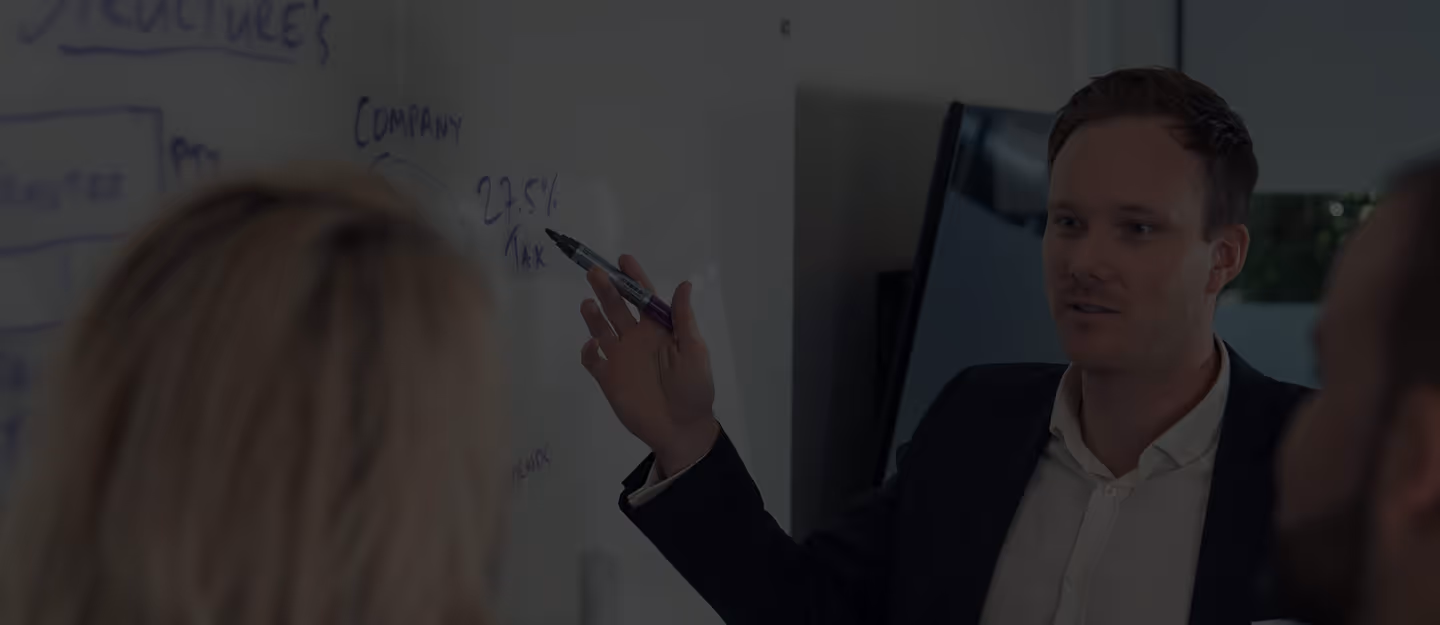 Professional presenting ideas on a whiteboard during a team meeting, gesturing with a marker while colleagues listen in an office setting.