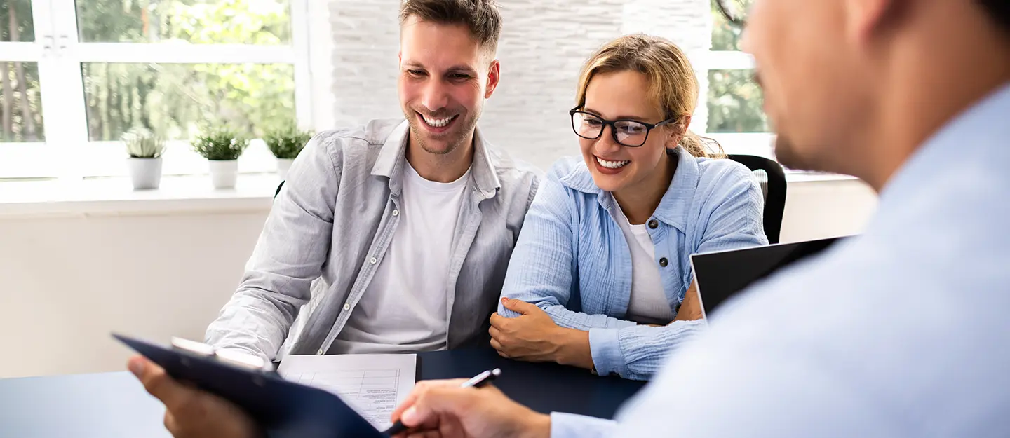 Smiling couple sitting at a desk reviewing documents with a professional across from them.