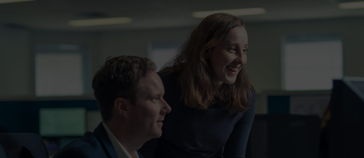 Two coworkers smiling and looking at a computer screen in an office environment.