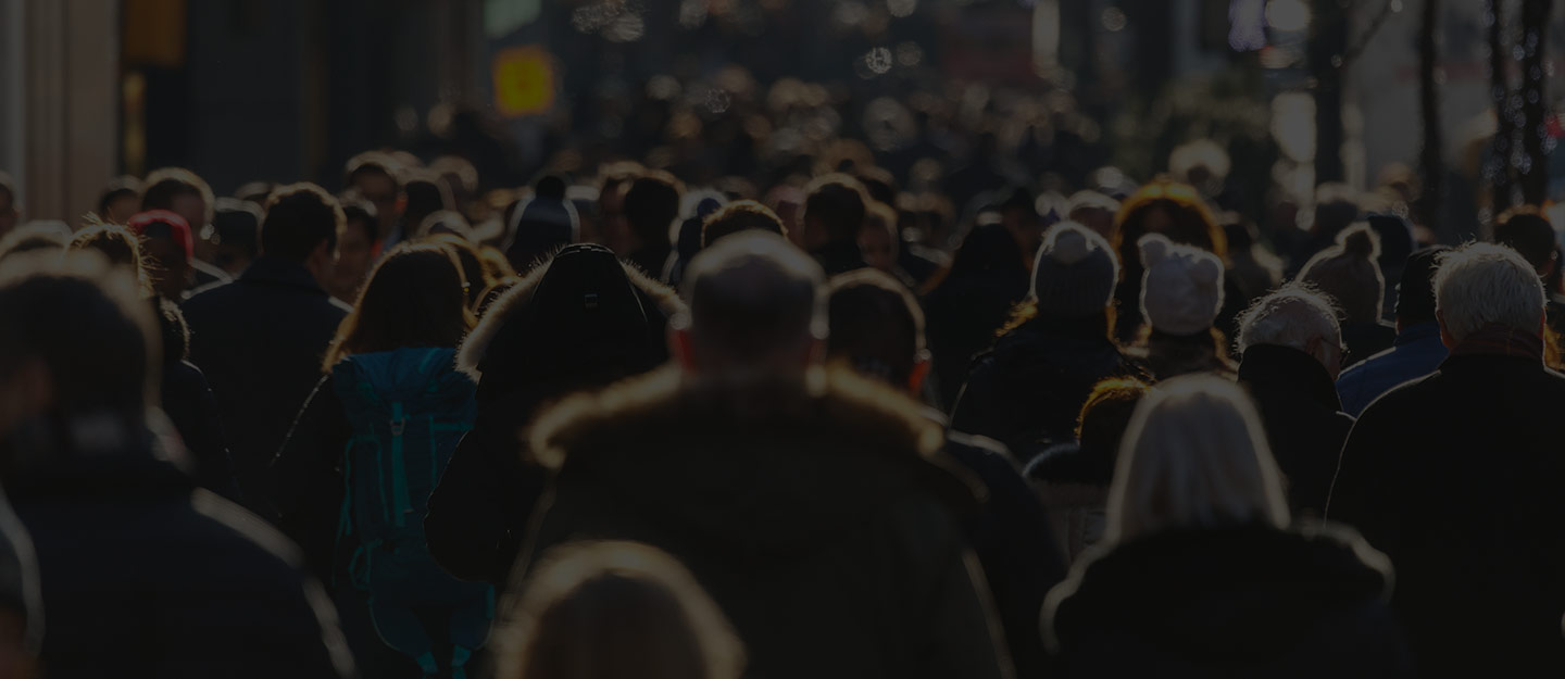 Crowd of people walking outdoors wearing winter coats and hats.