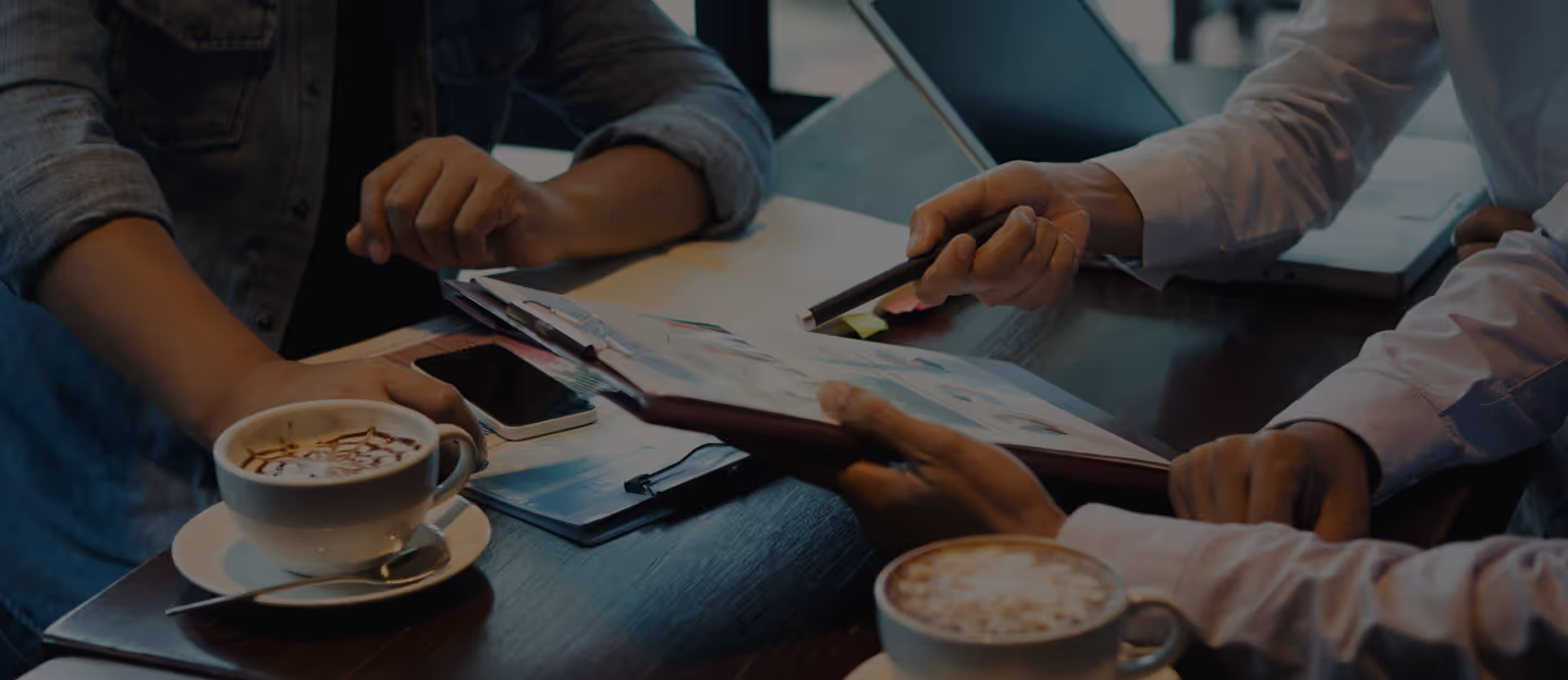 Two people sitting at a table with coffee, reviewing documents and a smartphone.