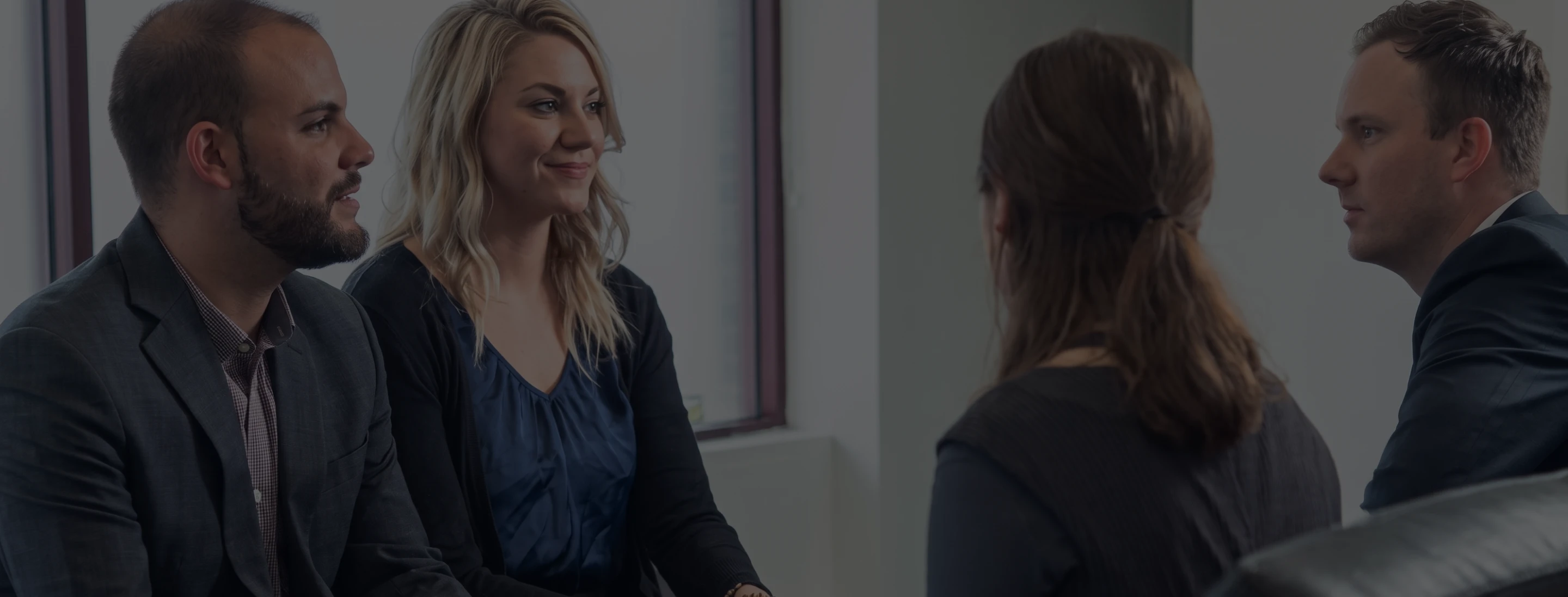 Two men and two women in a business meeting, facing each other and conversing in an office.