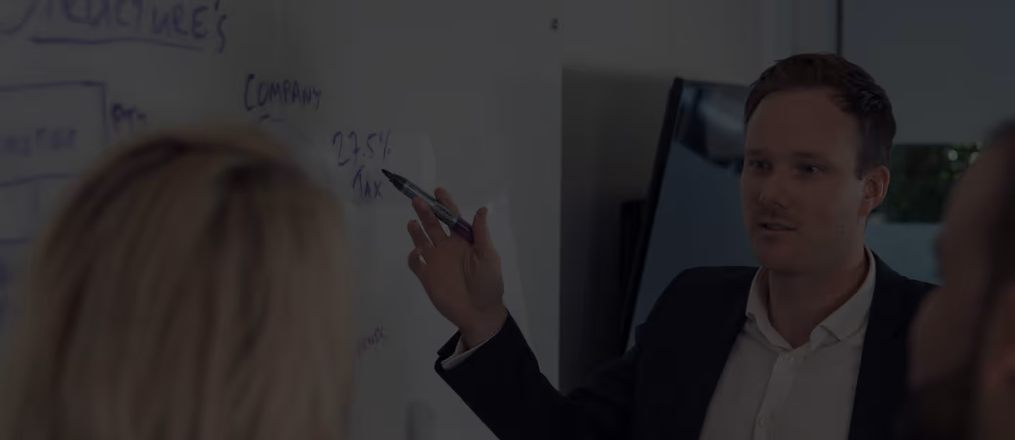 Someone writing in a notebook with a pen while planning notes sit open on a desk.