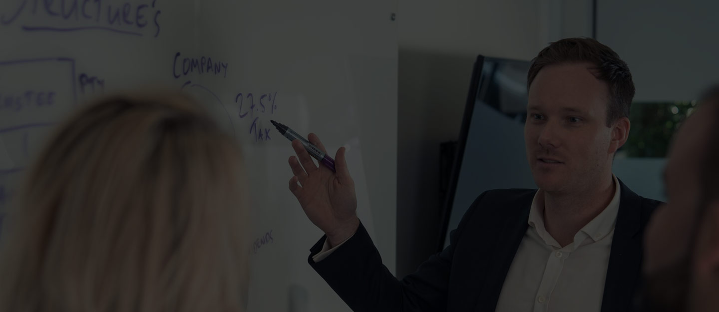Someone writing in a notebook with a pen while planning notes sit open on a desk.