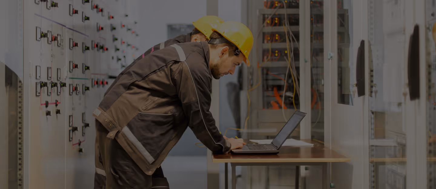 An electrician tightening or testing wiring at an open switchboard while wearing gloves.