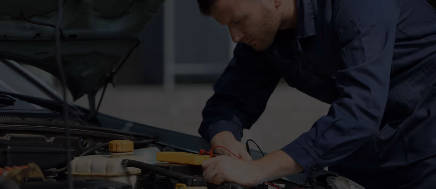 A mechanic reaching up to work on the underside of a car raised on a hoist.