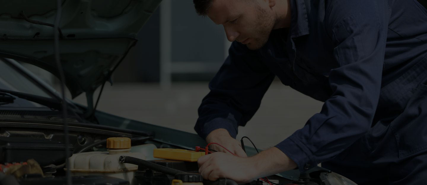 A mechanic reaching up to work on the underside of a car raised on a hoist.