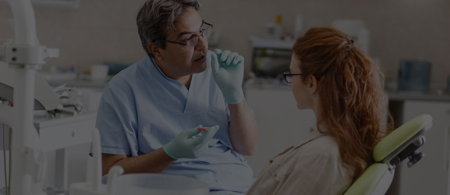 A dental clinician reaching for instruments beside a reclined patient chair.