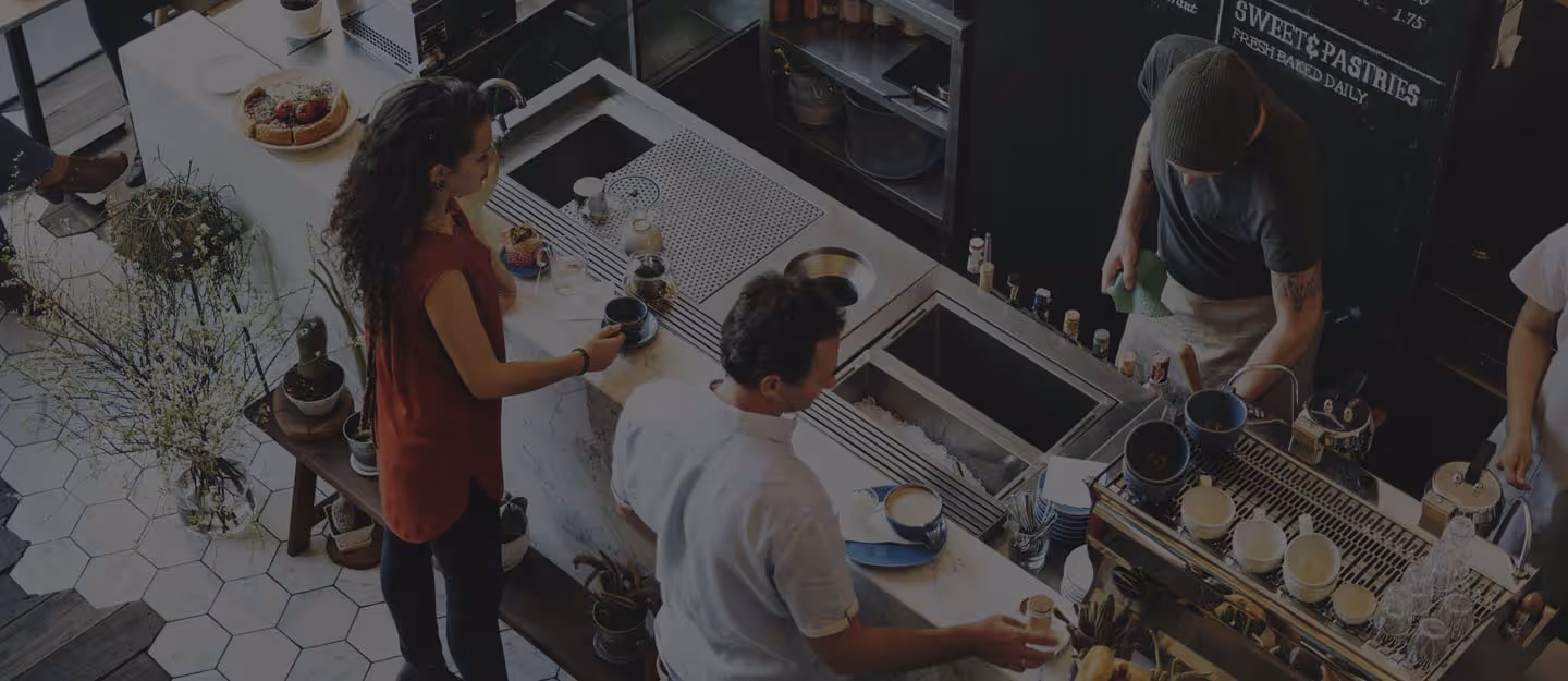 A barista steaming milk and working the espresso machine behind a busy counter.