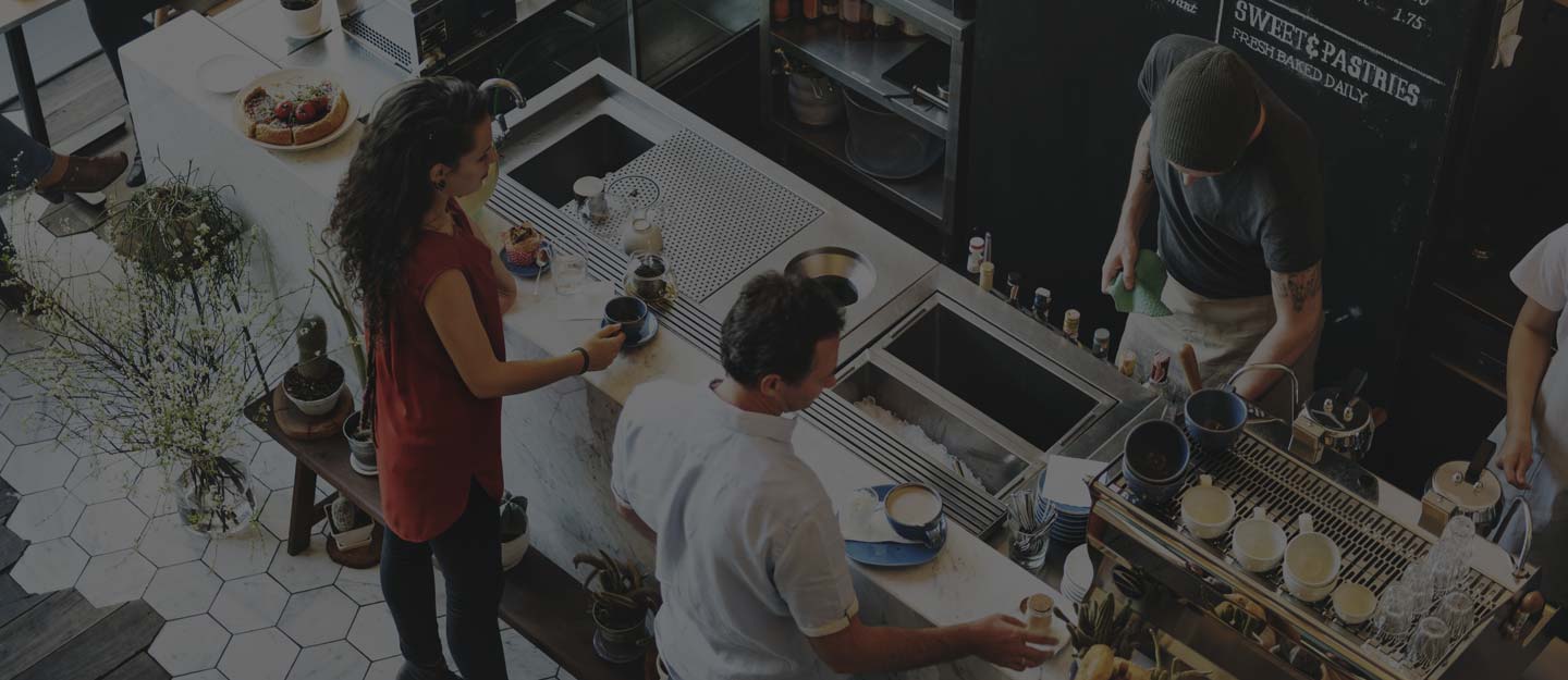A barista steaming milk and working the espresso machine behind a busy counter.