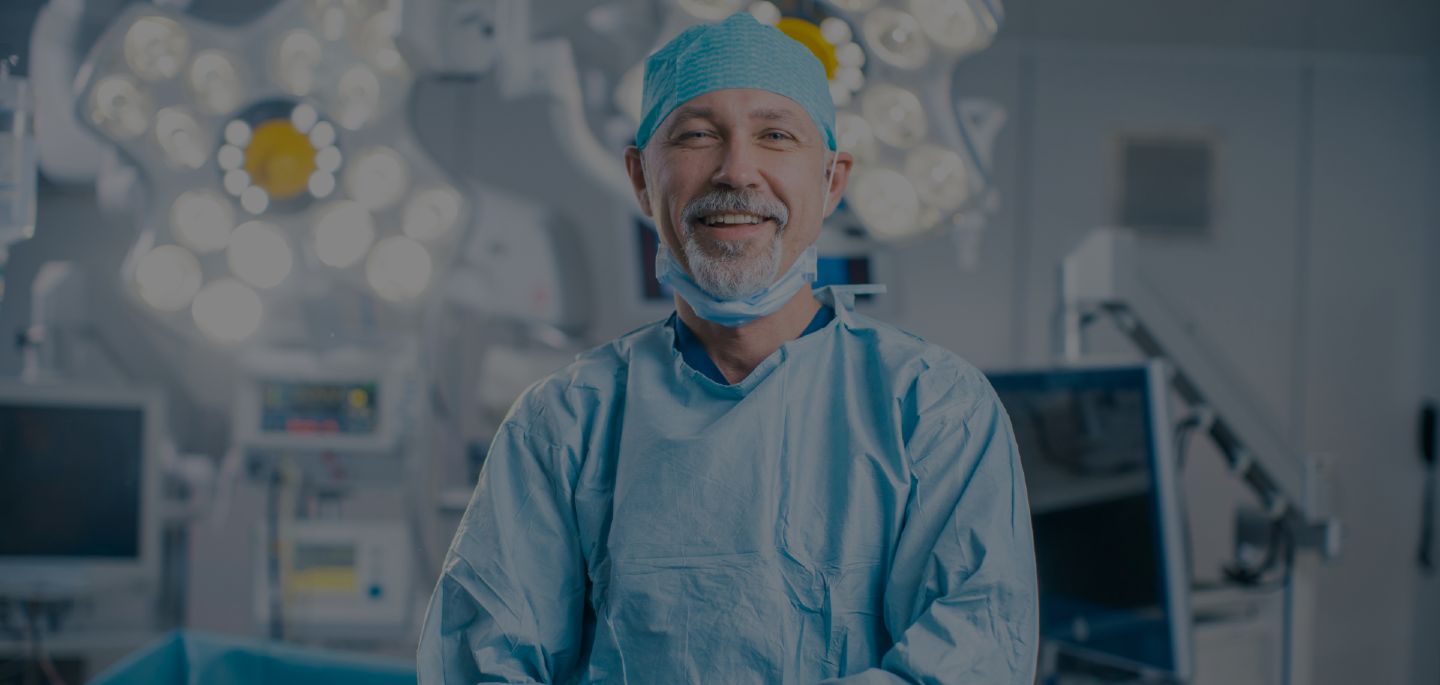 A figure in scrubs walking away down a long, brightly lit hospital corridor.
