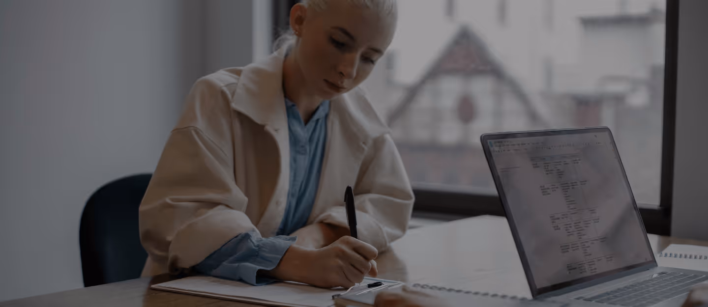Two people shaking hands firmly over a stack of signed sale contracts on a desk.
