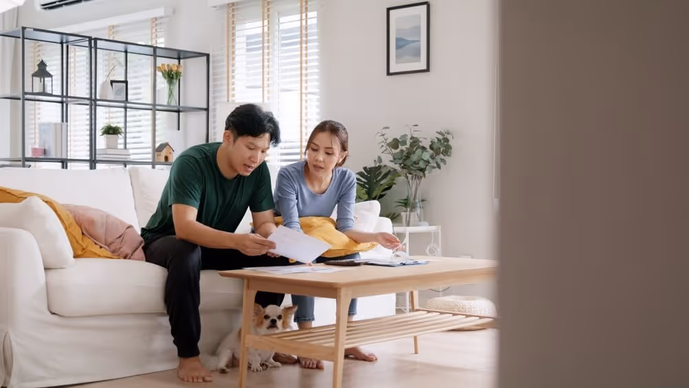 A young couple in their home, looking for their financial documents and trying to decide on a strategy together.