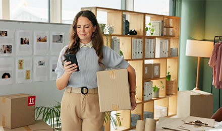 A young female holding boxes packed with work-from-home equipment, such as company laptops, for her staff.