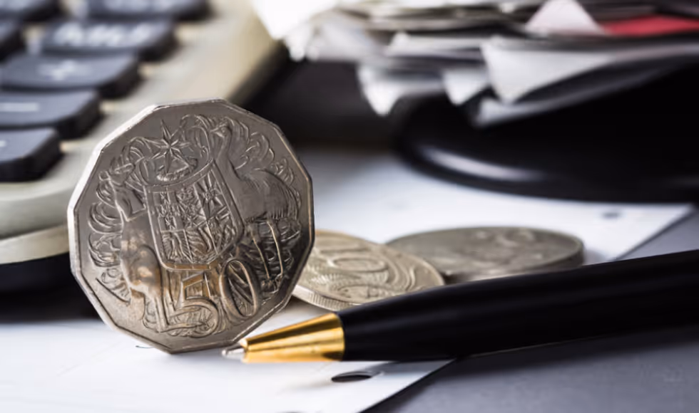 A closeup of an Australian 50 cent next to a pen and a calculator.