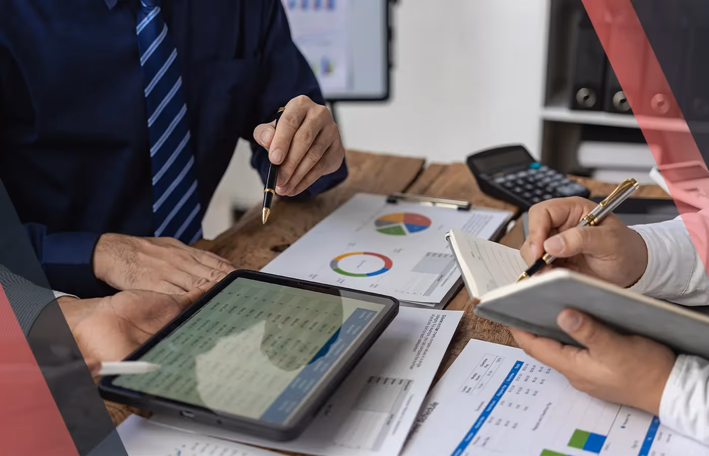 Two professionals discussing financial reports with a tablet, calculator, and notepad on a desk.