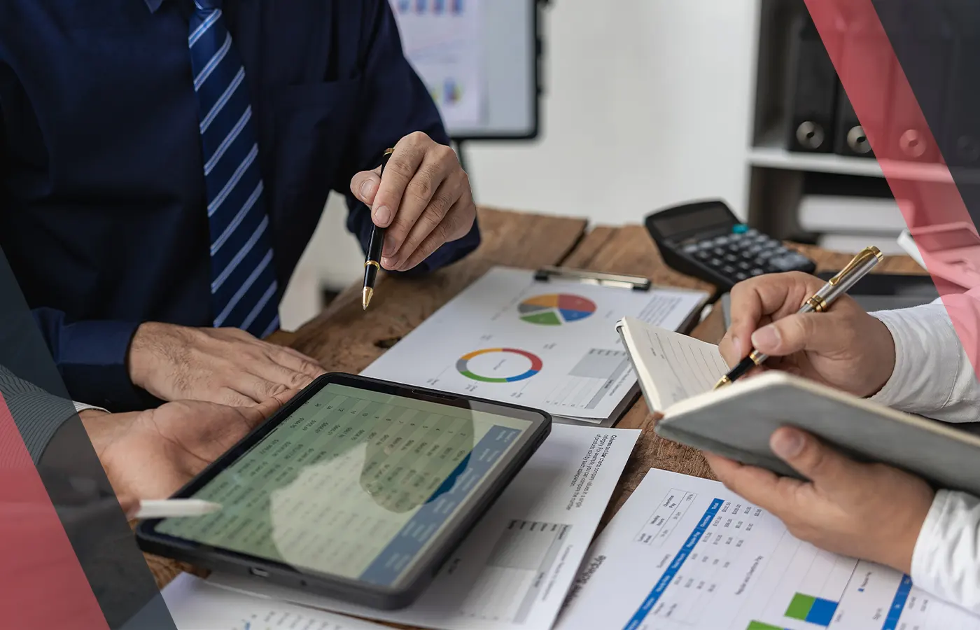 Two professionals discussing financial reports with a tablet, calculator, and notepad on a desk.