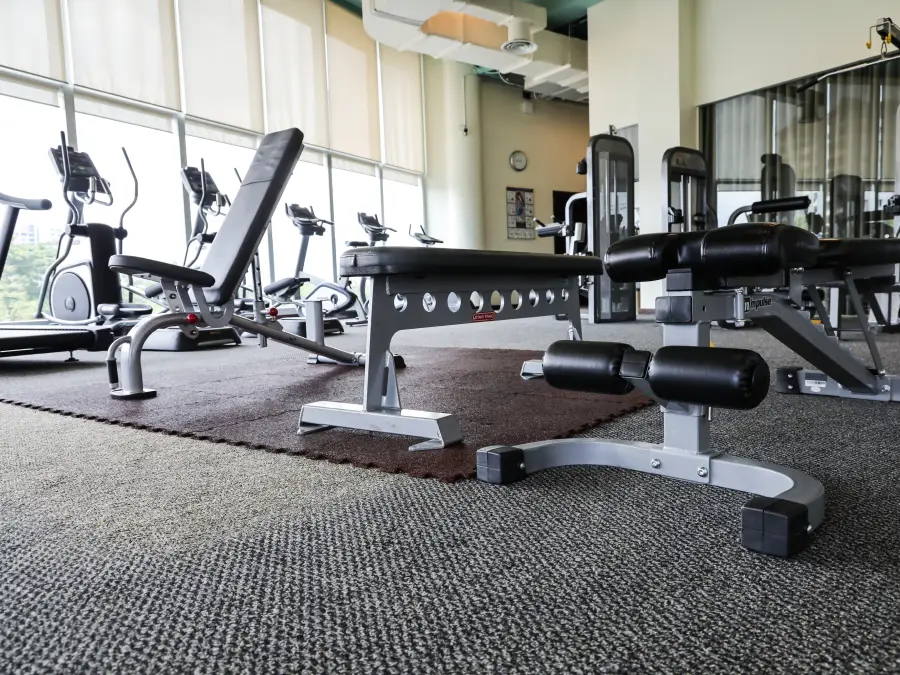 Modern hotel gym with treadmills and weight machines facing floor-to-ceiling windows with a bright city view.