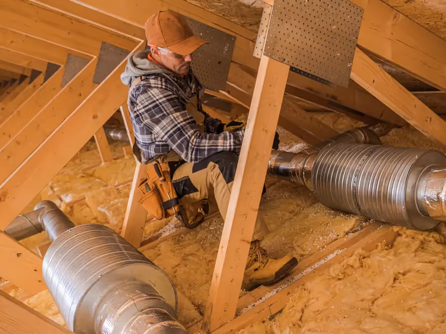 A tradesman working on an HVAC installation inside the attic 