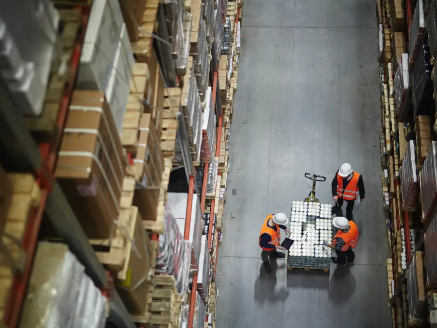 Above view of workers in large warehouse, inspecting goods on a cart.