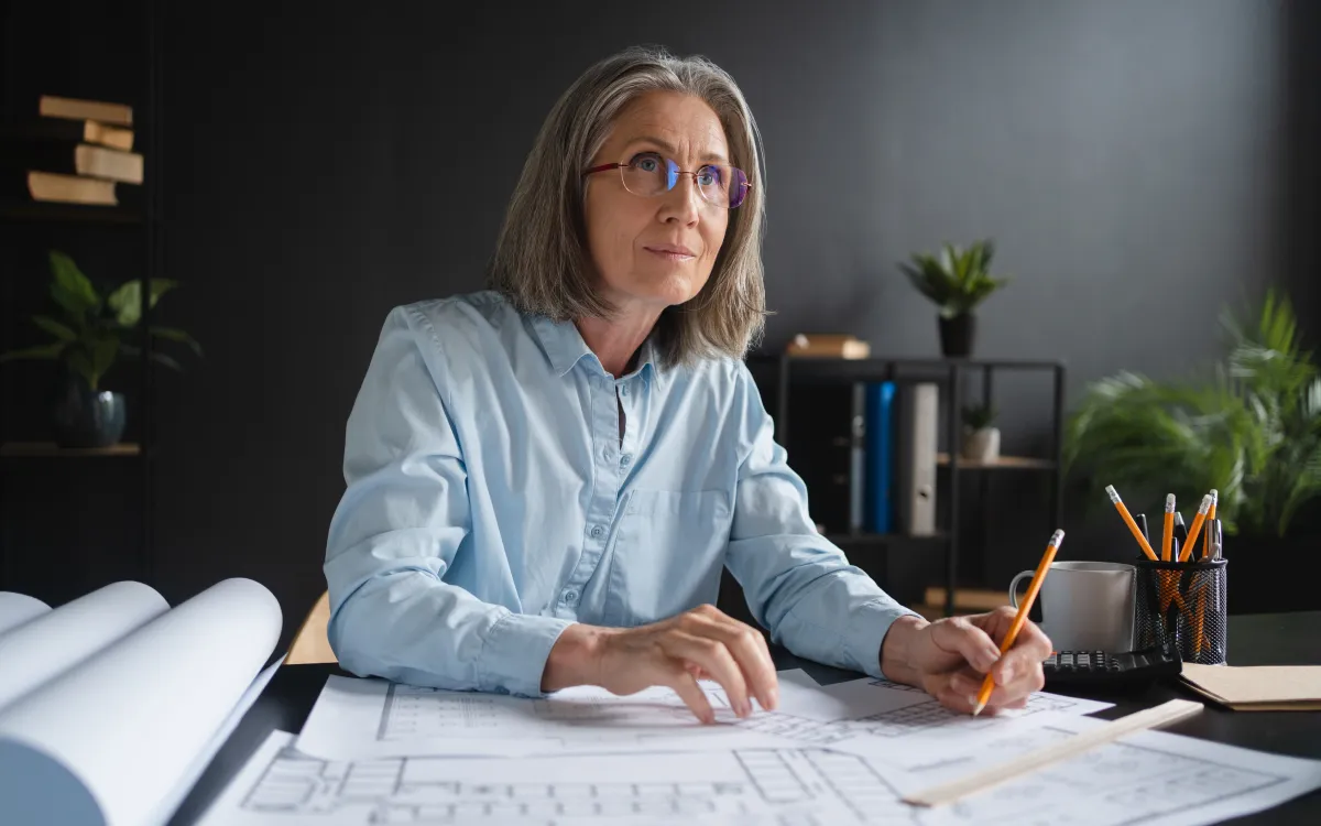 A female architect wearing glasses, working on an architectural blueprint.