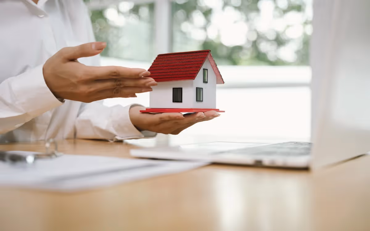 A close-up of hands during a real estate transaction, with a small scale model of a house.