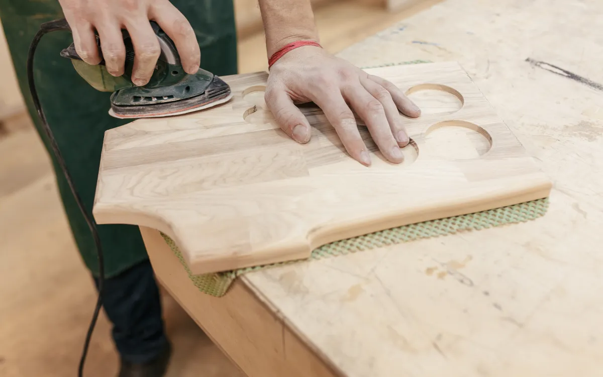 Close up of a hand holding a grinder, working on a cabinet plank