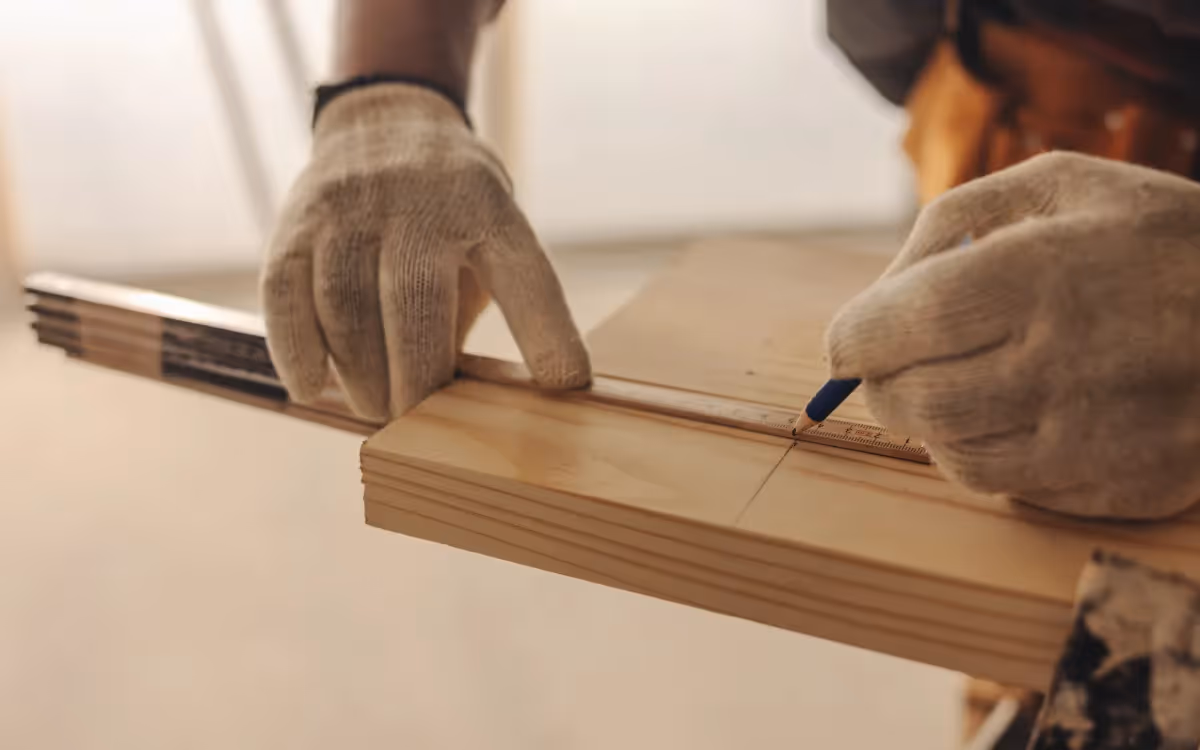 Close-up of a gloved hand, measuring a wooden plank