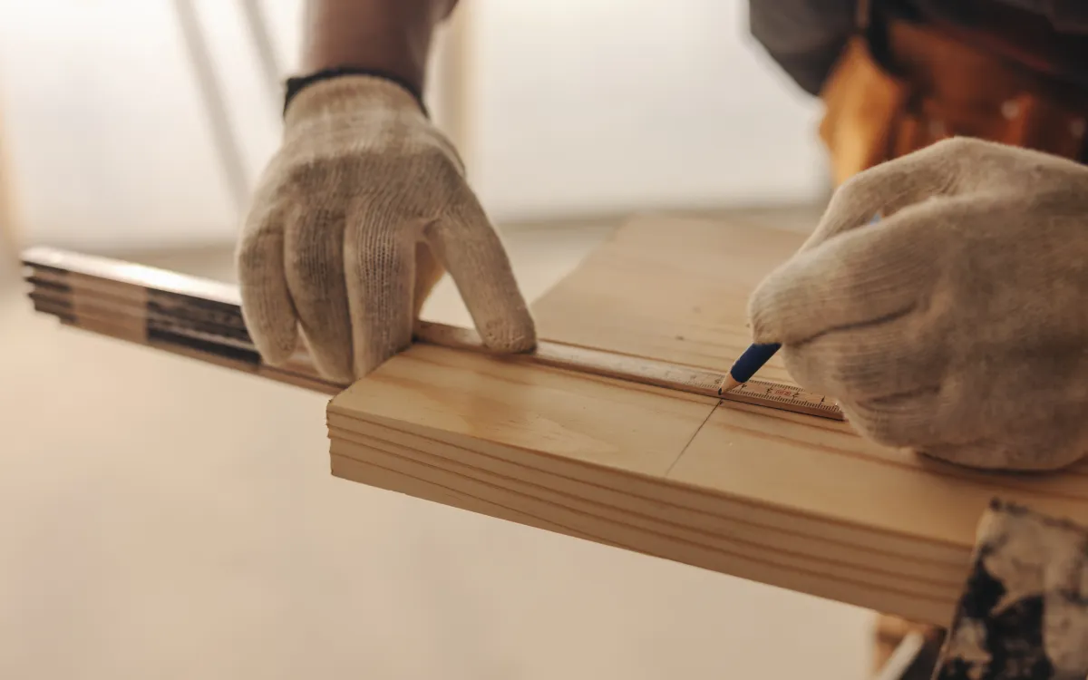 Close-up of a gloved hand, measuring a wooden plank