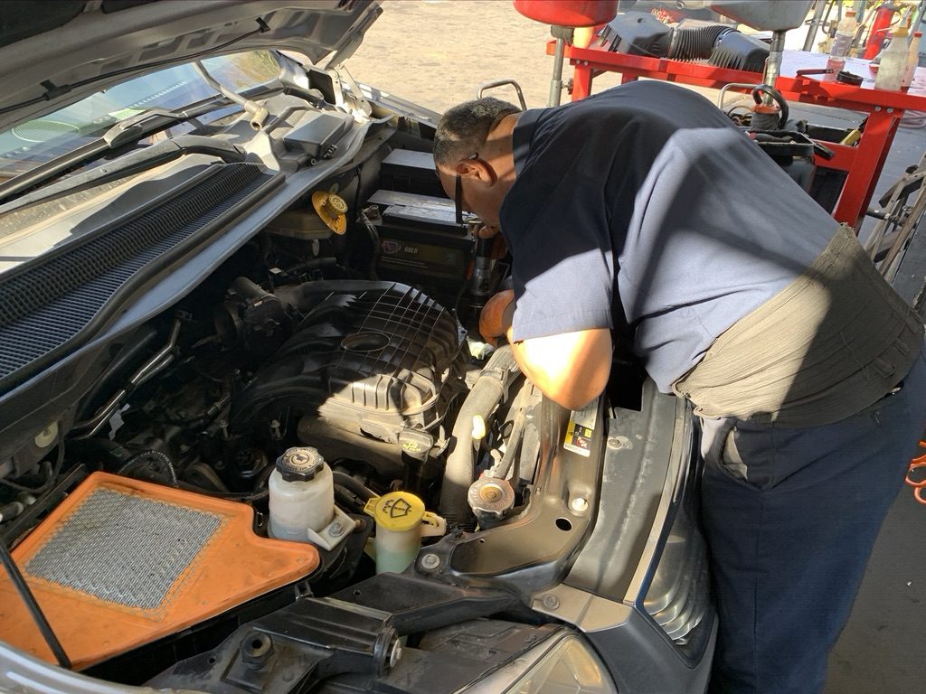 Dirty engine air filter pulled out for inspection while a Quality Tune-Up technician works in the engine bay
