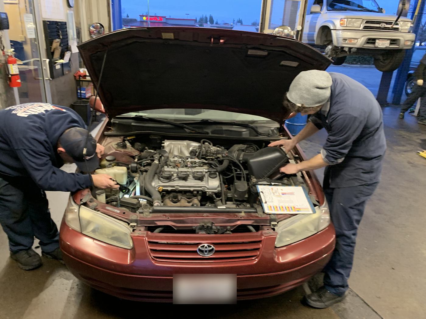 Two Quality Tune-Up technicians working on the engine of a Toyota Camry