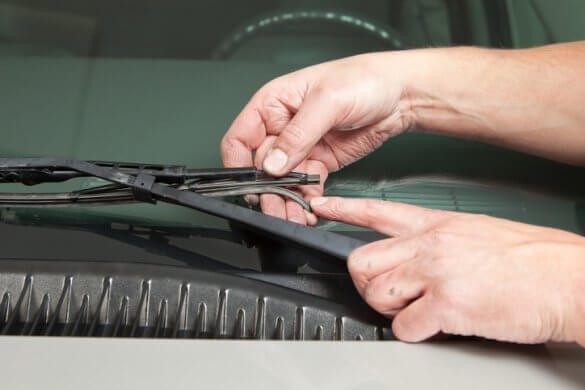 Hand lifting a worn windshield wiper blade off the glass to check the rubber edge