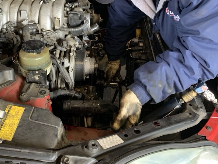 Gloved technician tracing engine wiring near the belts on a V6 engine