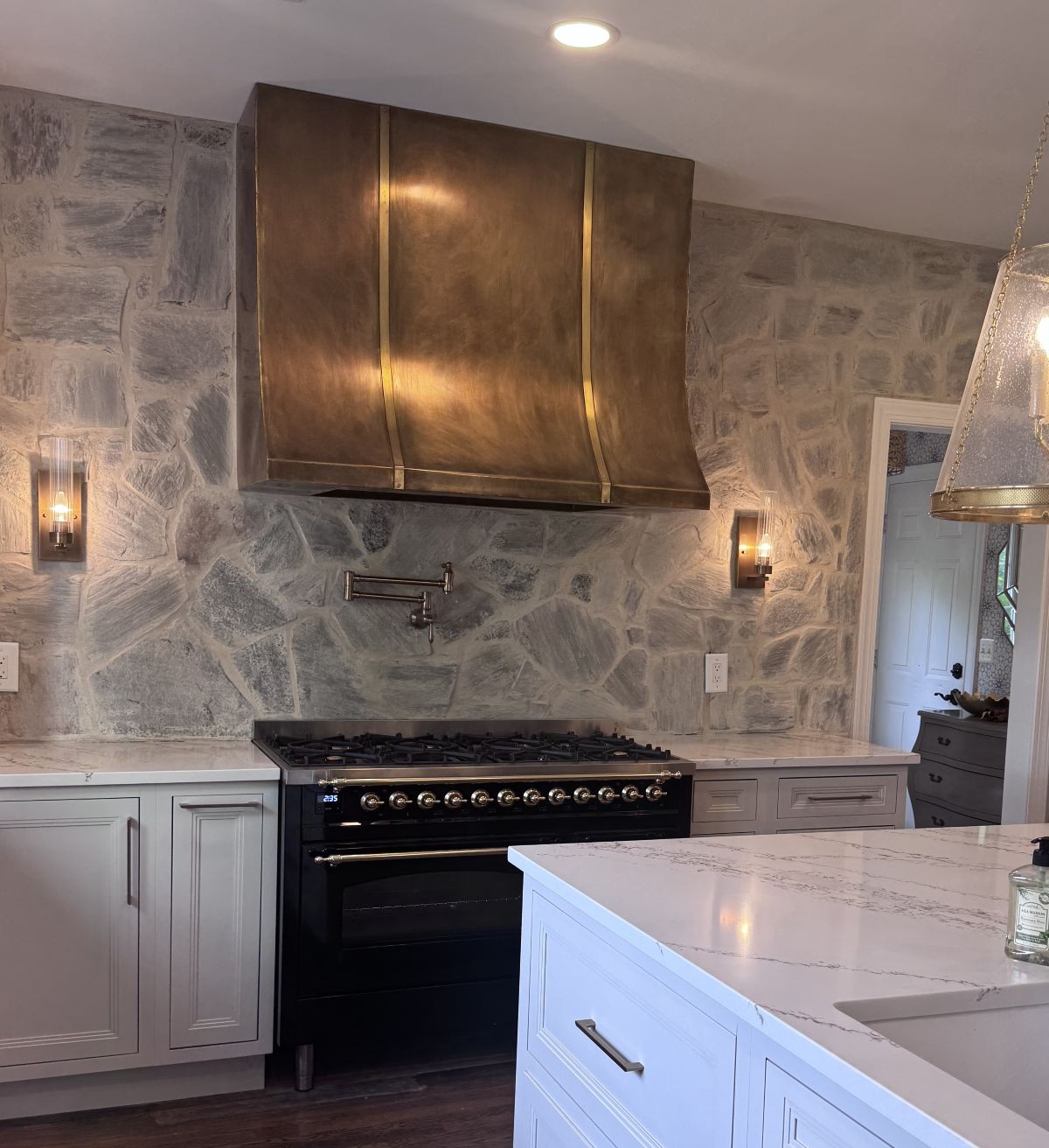 lifestyle image of Handcrafted brass range hood with vintage patina finish and vertical brass accents