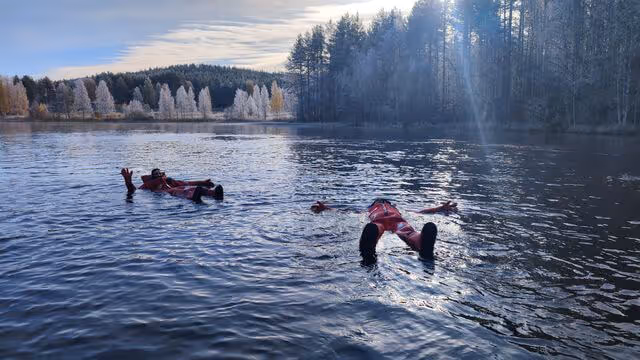 Capturing the reflective beauty of an autumn lake in Lapland with a guest in a floating suit enjoying the serene environment.