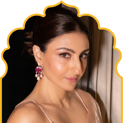 Woman with dark hair styled in a low bun wearing pink earrings and a sleeveless outfit, looking slightly to the side.