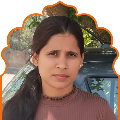 Woman with long dark hair tied back, wearing a brown top, standing outdoors near a tree and a car.