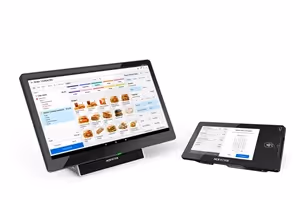 Two black touchscreen devices displaying a quick service restaurant ordering interface with menu items and payment options.