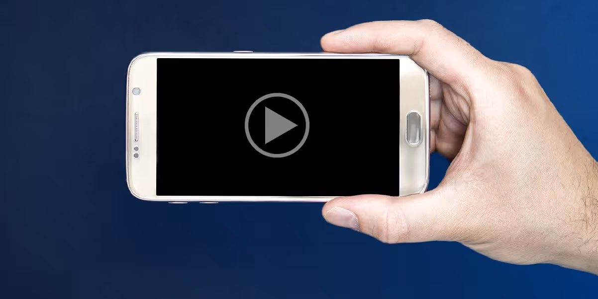 Image of a man's hand holding a smart phone with a video loaded and ready to play on the screen.